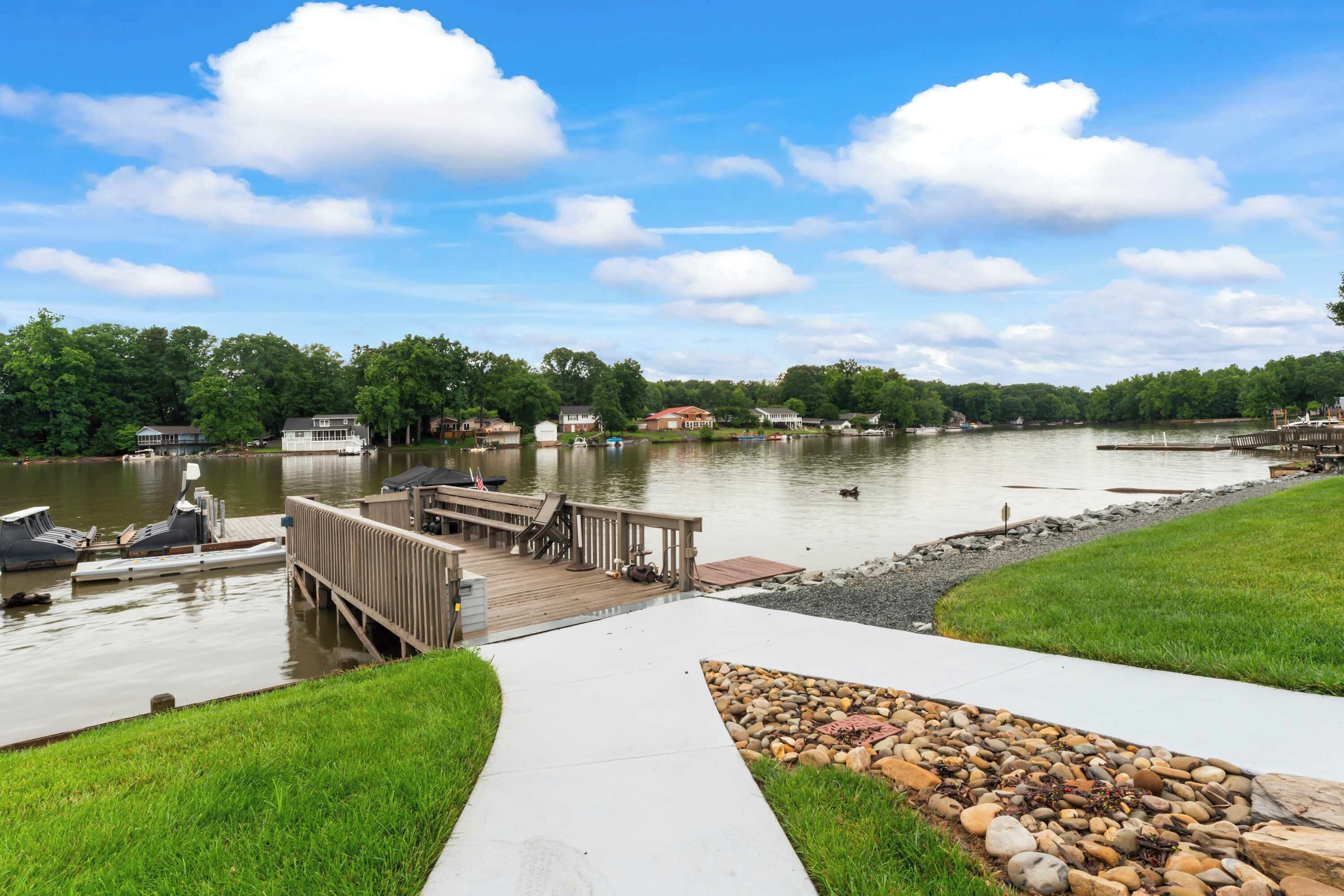 A lakeside property with a dock, boats, and a grassy area with a stone pathway.