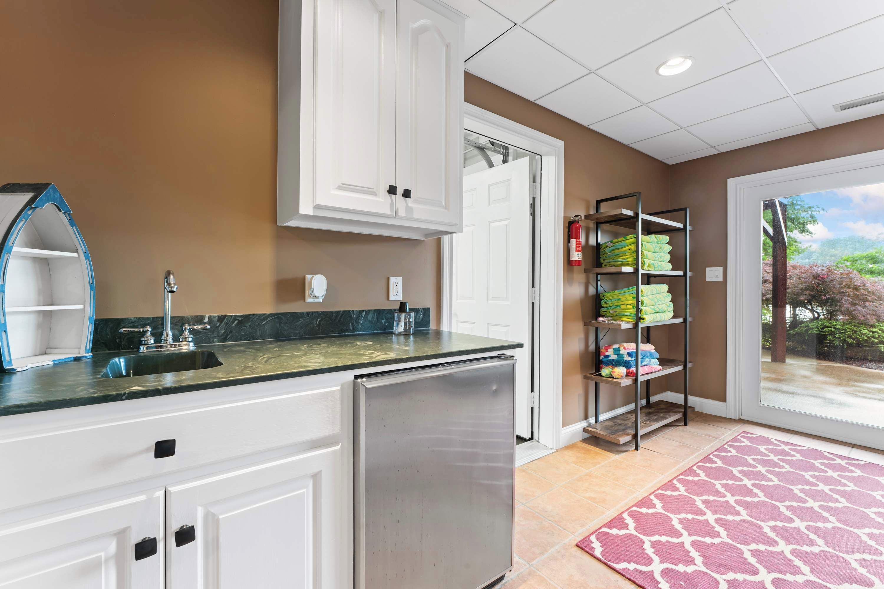 A kitchen with white cabinets, a stainless steel refrigerator, a marble countertop, and a red patterned rug.