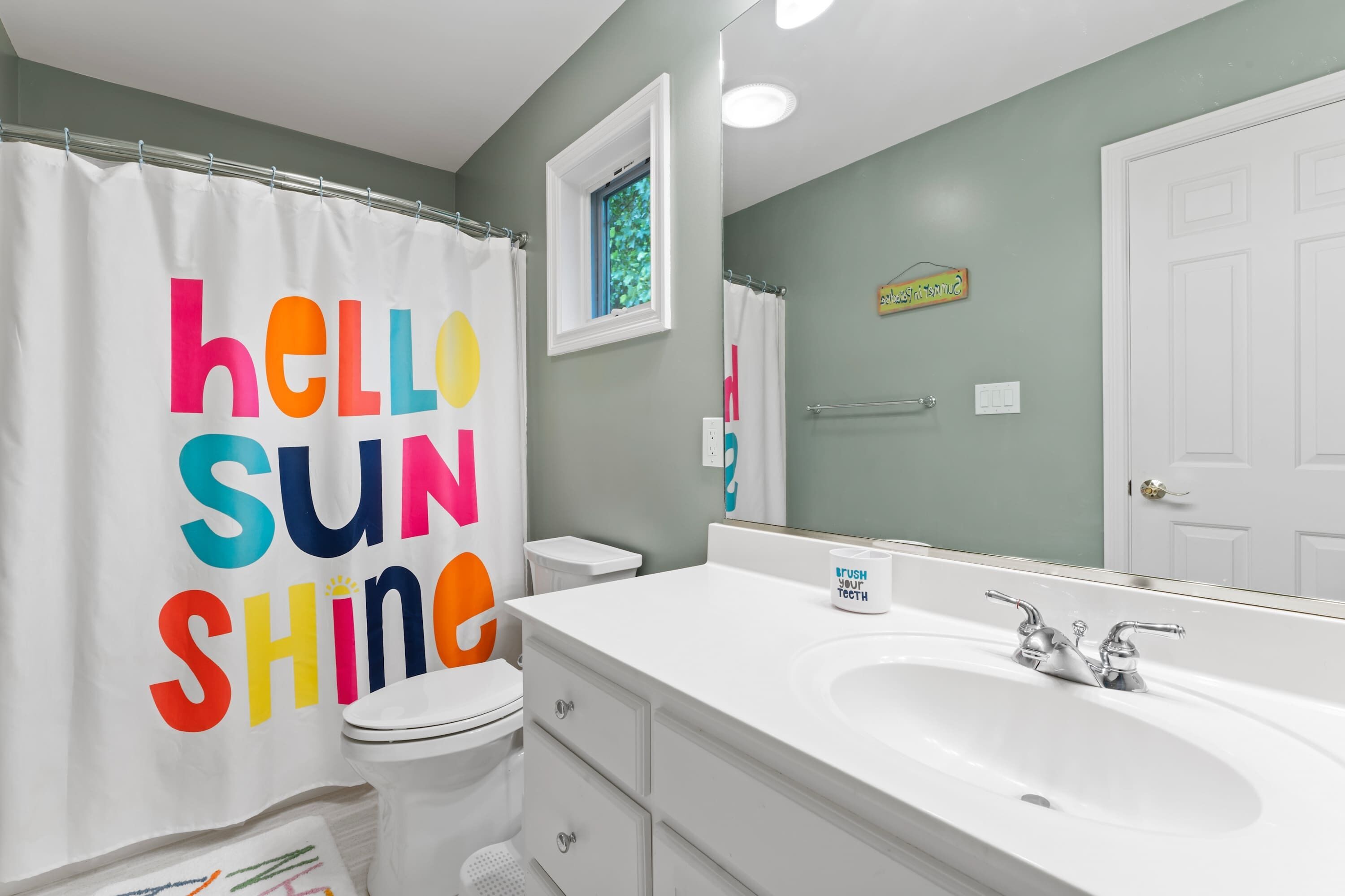 A bathroom with a white sink, a mirror, a toilet, and a shower curtain with colorful text.