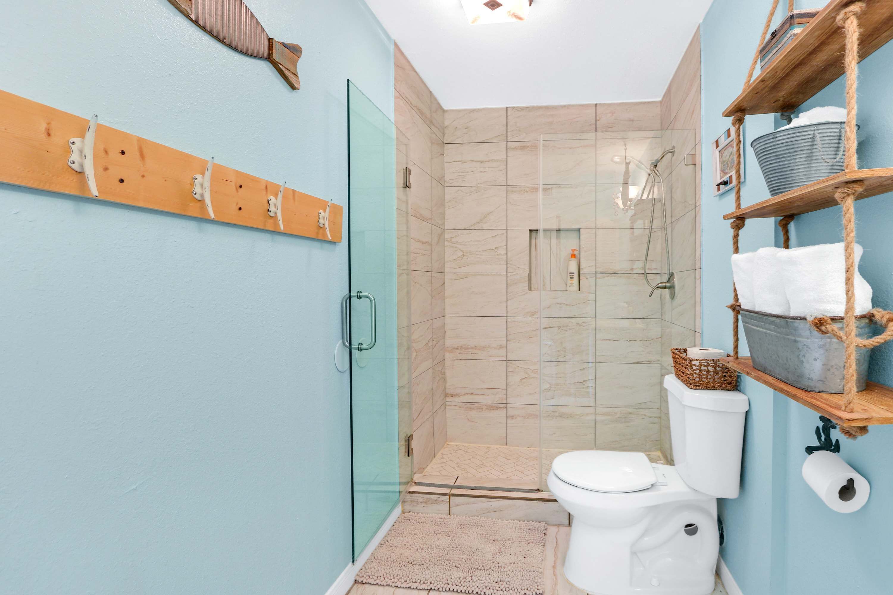 Een badkamer met een douchecabine van glas, een toilet en een plank met handdoeken en toiletartikelen.