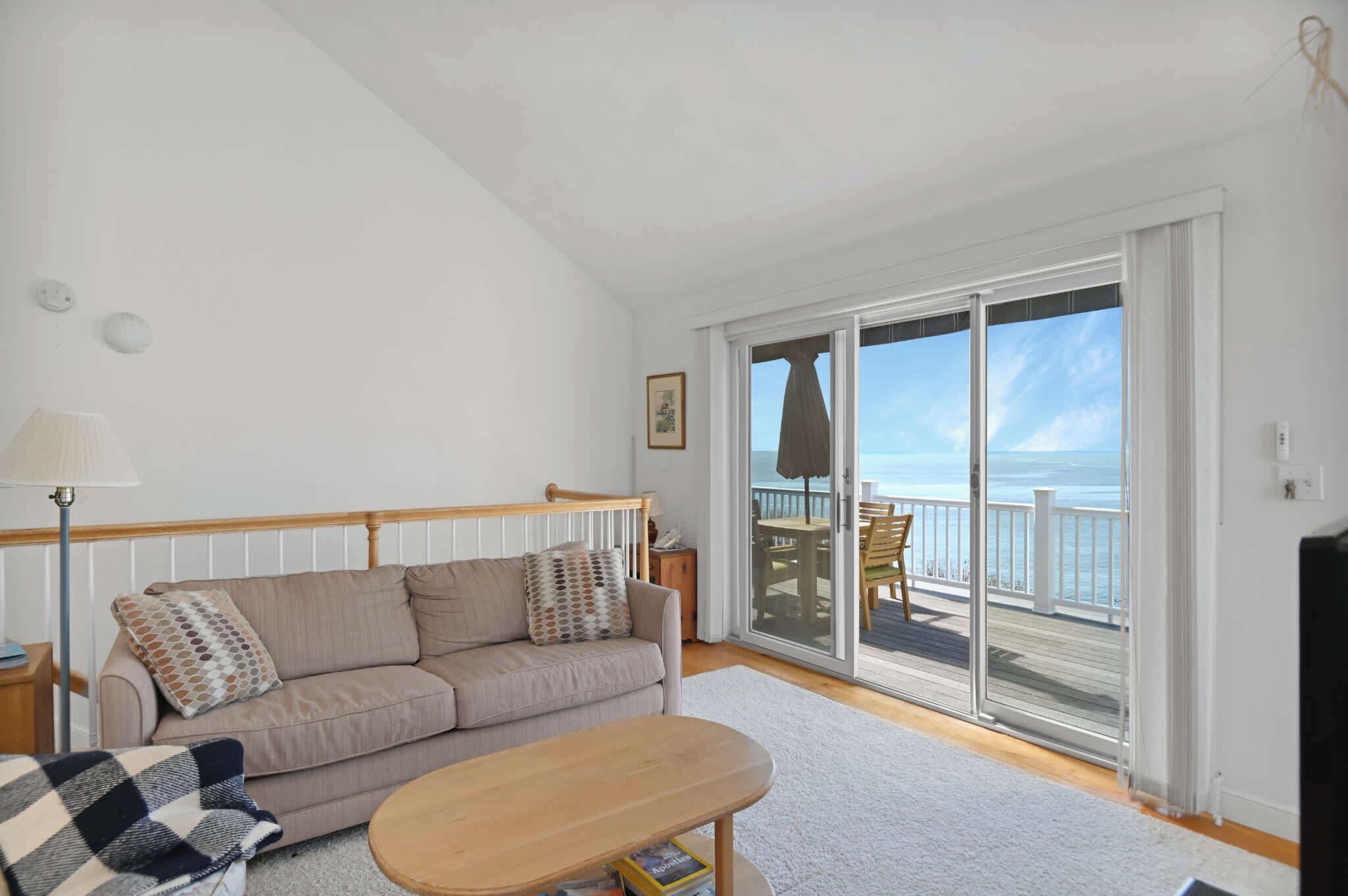 A living room with a sofa, a coffee table, and a view of the ocean through large sliding glass doors.