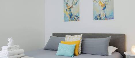A neatly made bed with a grey headboard, two pillows, and a folded towel on the side.