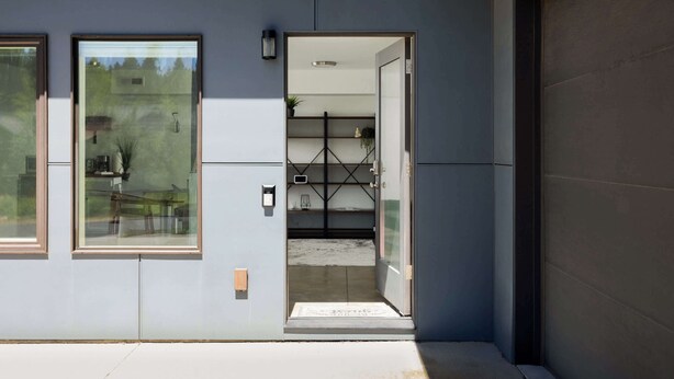 A modern building entrance with a glass door, a small outdoor seating area, and a visible interior with shelves and a plant. - 20 Min to Mt Bachelor! Perfect Basecamp for Skiers (Bend)