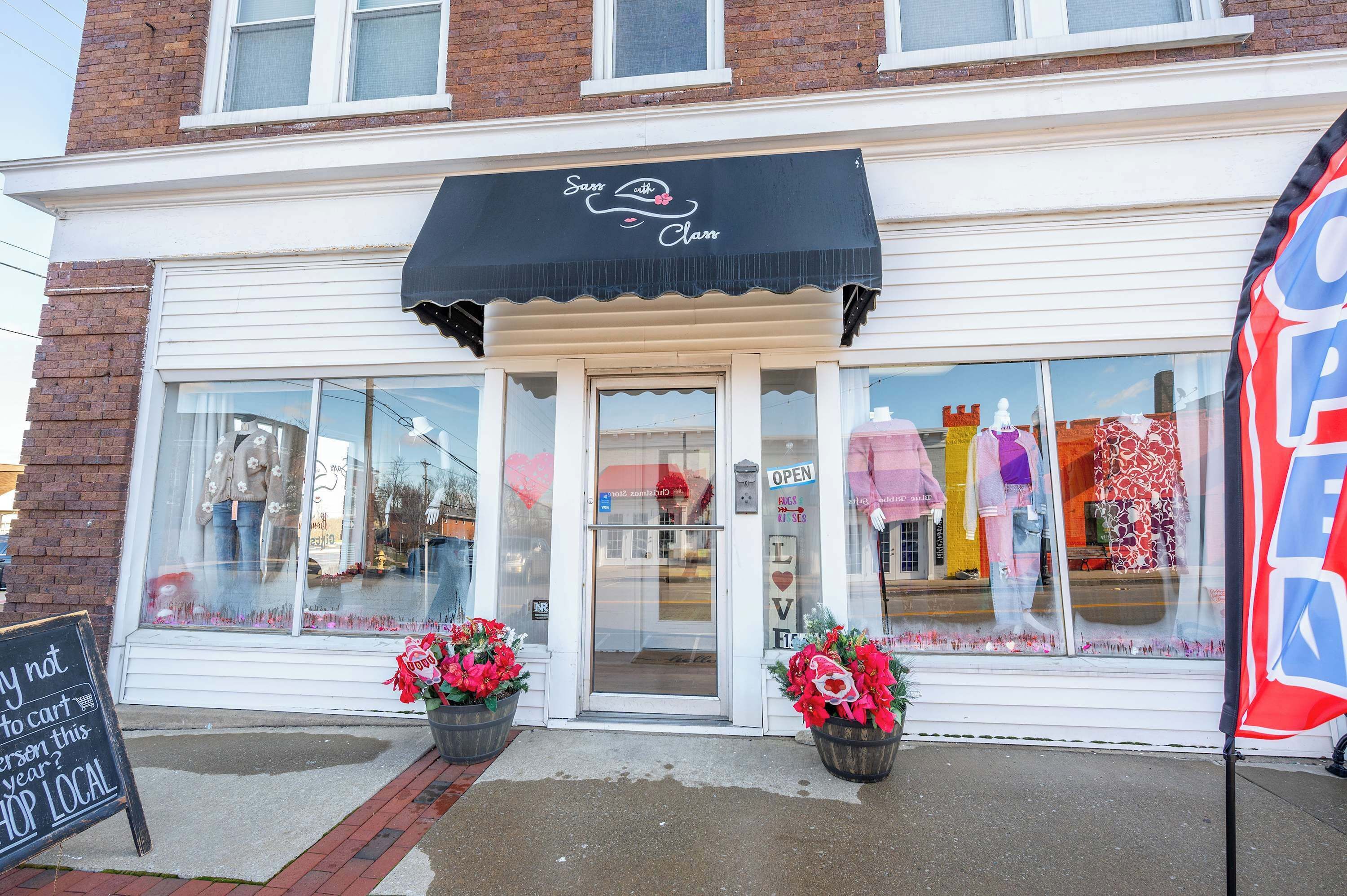 A storefront with a black awning, large windows, and two potted plants.