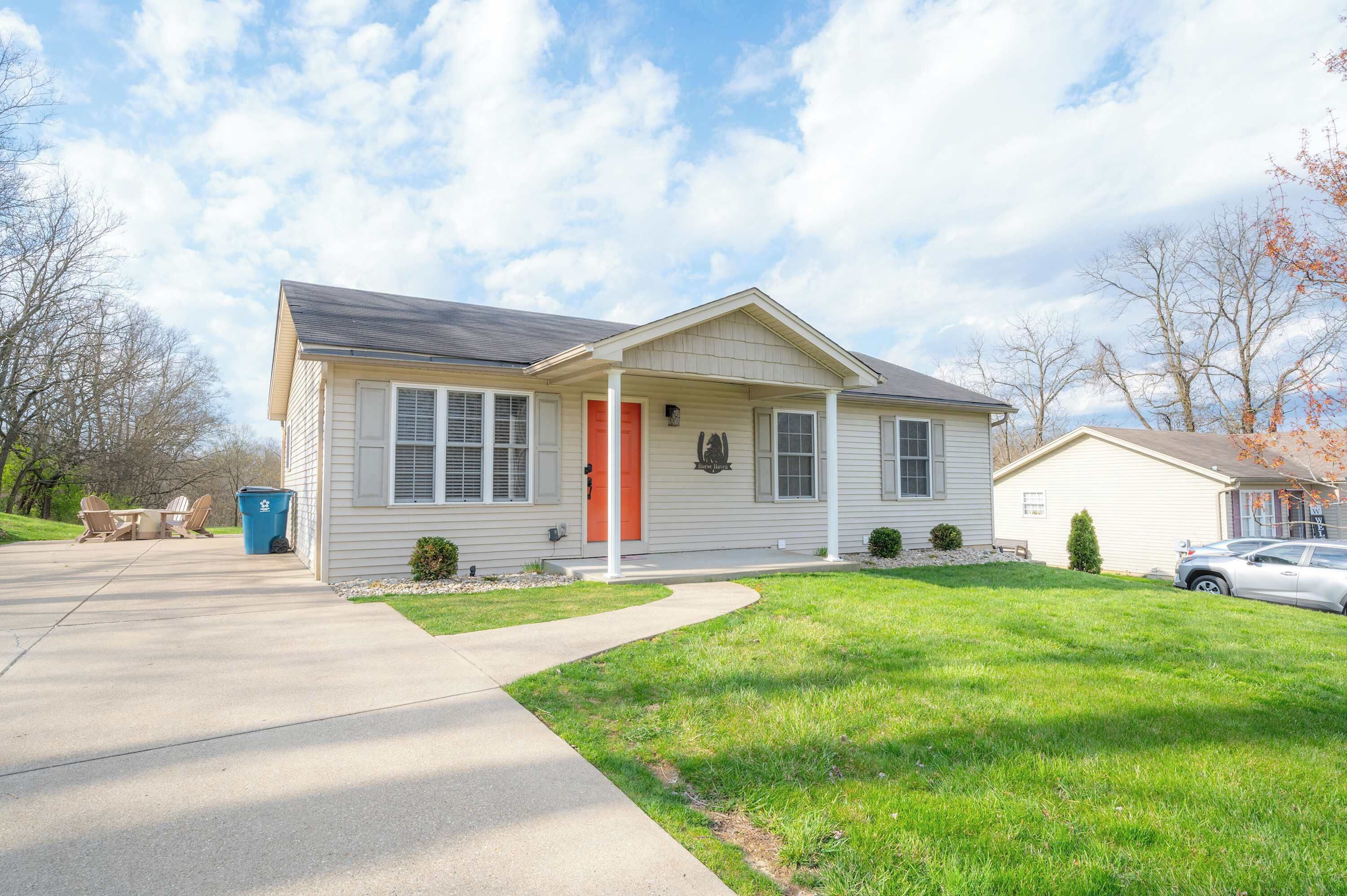 A single-story house with a red door, a covered porch, and a small front yard.