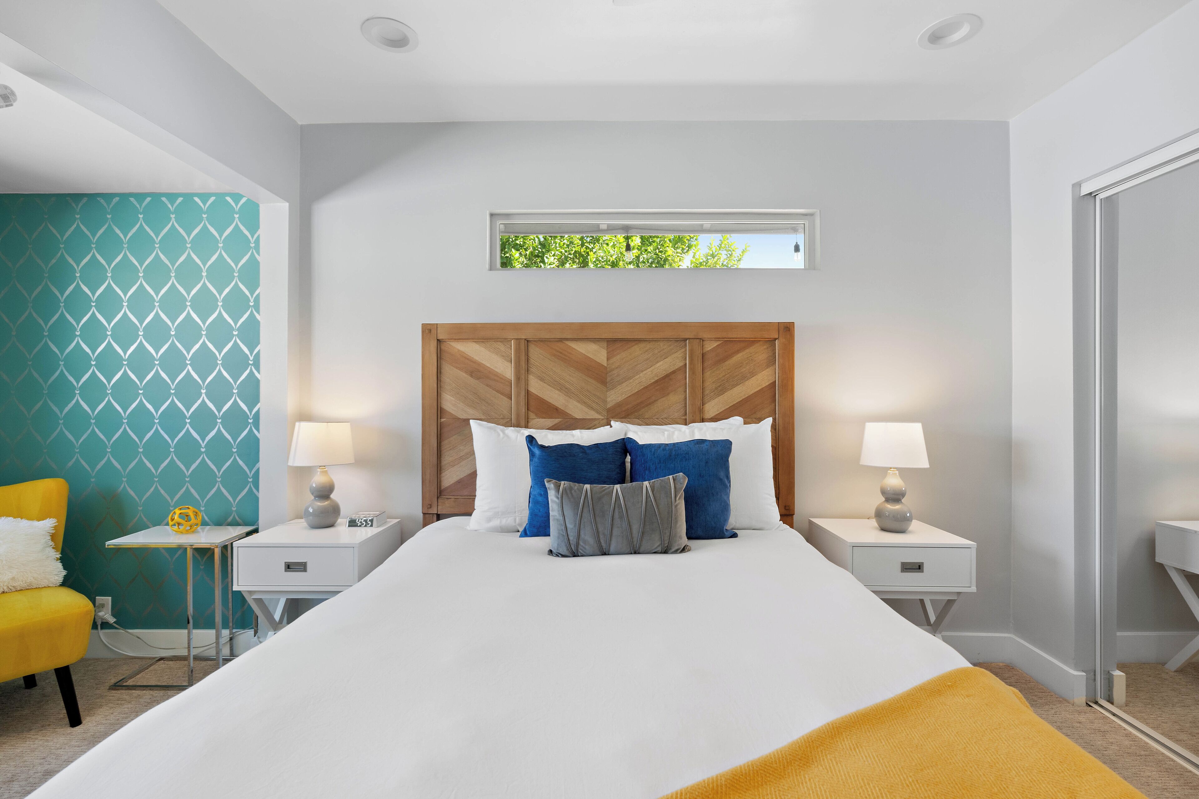 A modern hotel room with a large bed, two bedside tables, a small side table, and a window with a view of greenery.