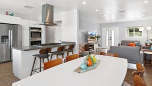 A modern kitchen with a central island, bar stools, and a dining table with a decorative centerpiece. - The Zen Space Private Pool! (Palm Springs)