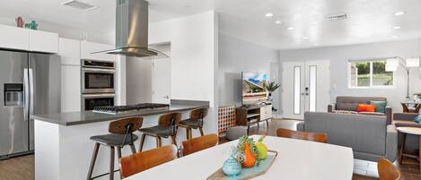 A modern kitchen with a central island, bar stools, and a dining table with a decorative centerpiece.