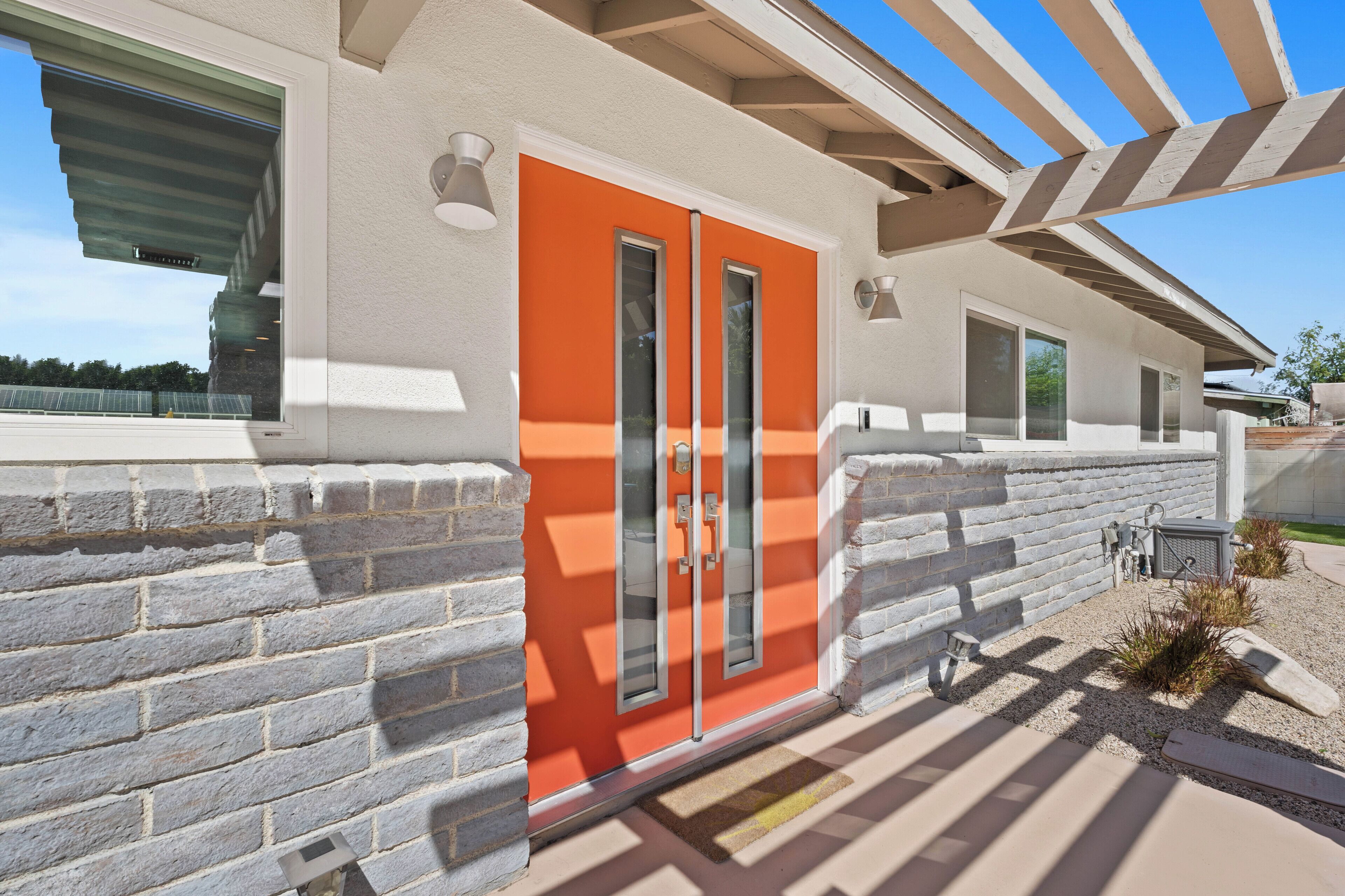 Un edificio moderno con una puerta naranja distintiva, paredes de piedra y un patio cubierto.