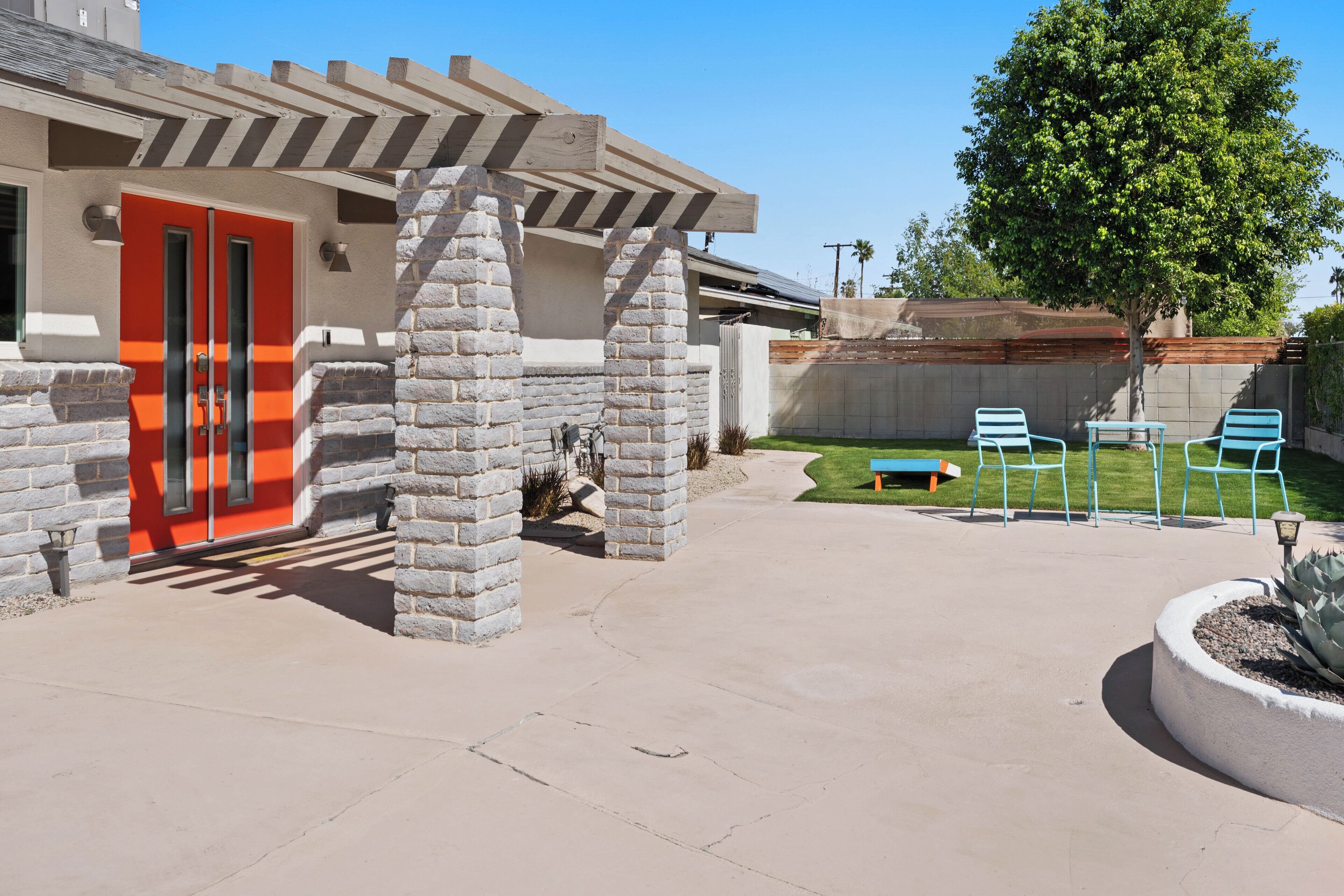 A patio area with a stone wall, a red door, and blue chairs.