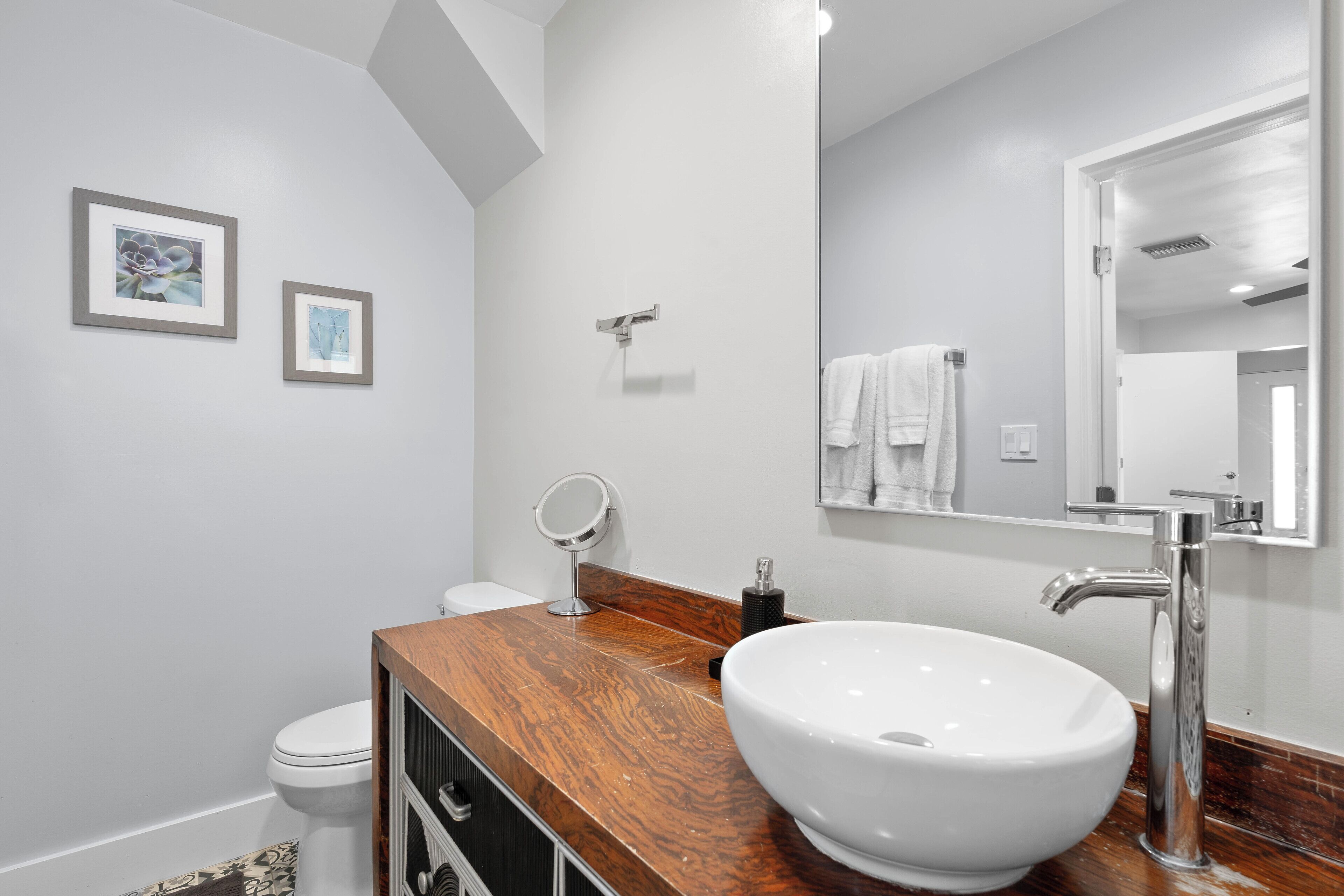 A modern bathroom with a wooden vanity, a white sink, and a large mirror.