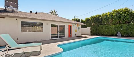 A modern house with a swimming pool, a red door, and a large window.