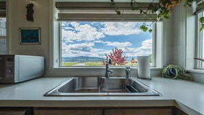 A kitchen with a stainless steel sink, a microwave, and a window with a view of a tree and landscape. - Hollenback Heights Epic Views! (Eureka)