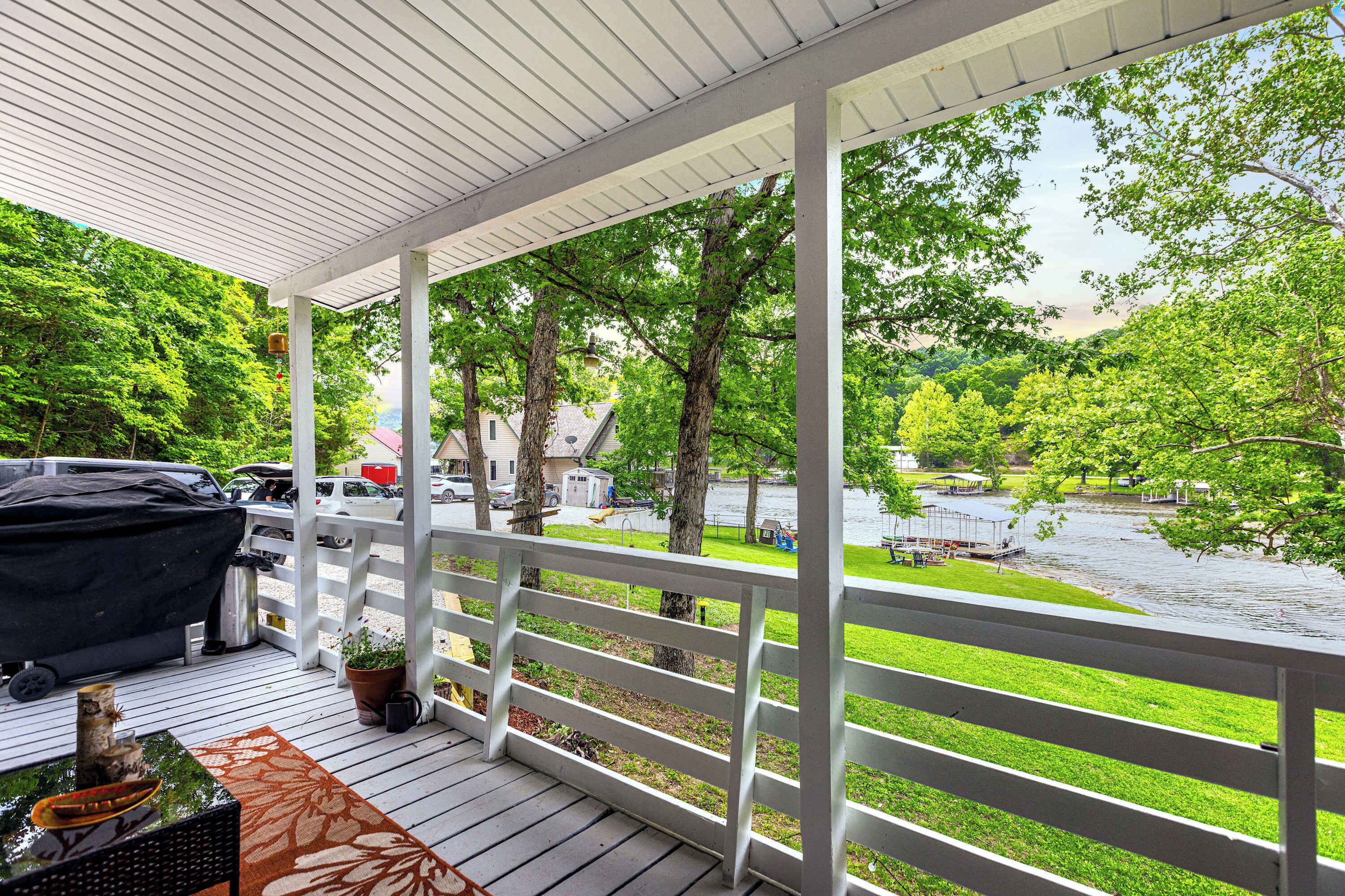 A covered outdoor deck with a grill, seating, and potted plants.