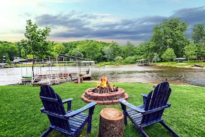 Eine Uferterrasse mit Feuerstelle, zwei Adirondack-Stühlen und einem Steg mit Booten.