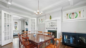 A spacious dining room with a large wooden table and chairs, a chandelier, and a fireplace. - Urban Elegance Getaway (Columbus)
