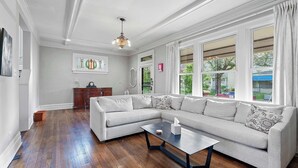 A living room with a sectional sofa, a coffee table, and large windows with curtains. - Urban Elegance Getaway (Columbus)