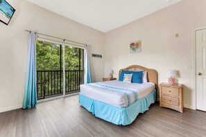 A bedroom with a large window, a bed with a blue bed skirt, a nightstand with a lamp, and a door.