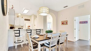 A dining area with a wooden table and white chairs, a kitchen with white cabinets, and a hanging light fixture. - Timeless Magic At Bahama Bay (Davenport)