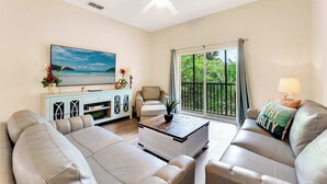 A living room with a sofa set, a coffee table, a TV, and a view of greenery through a window. - Timeless Magic At Bahama Bay (Davenport)