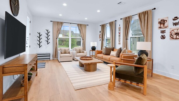 Un salon moderne doté d’un téléviseur à écran plat, de meubles en bois, d’un ensemble de canapés et d’une grande fenêtre agrémentée de rideaux.