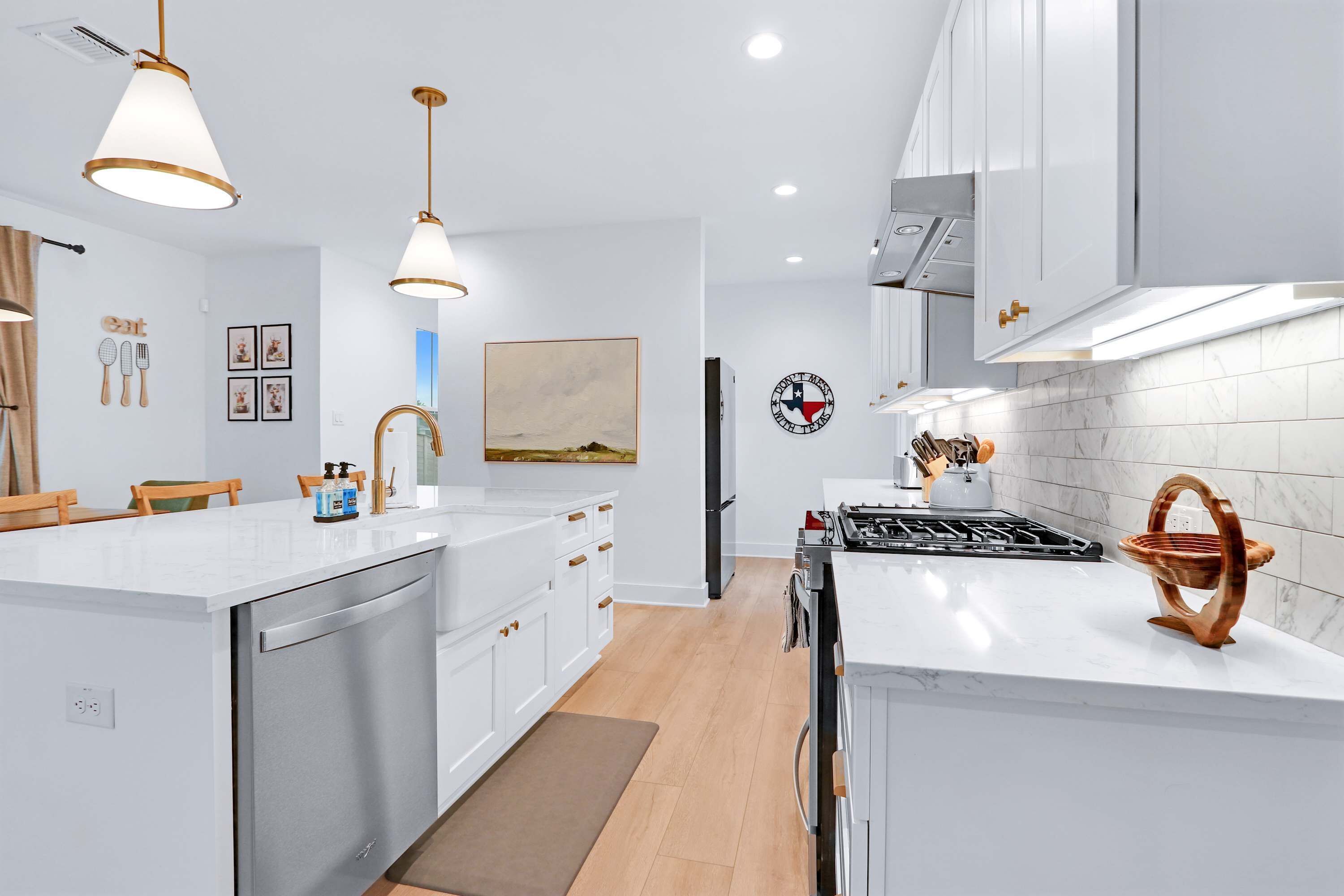 Una cocina moderna con armarios blancos, electrodomésticos de acero inoxidable, iluminación colgante y una isla central.