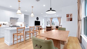 Une cuisine moderne avec des meubles blancs, une table à manger en bois et des luminaires suspendus.