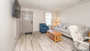 A living room with a grey sofa, a blue armchair, a wooden coffee table, and a white armchair. - Arkstone Retreat 2 - 4 minutes from the Ark! (Williamstown)