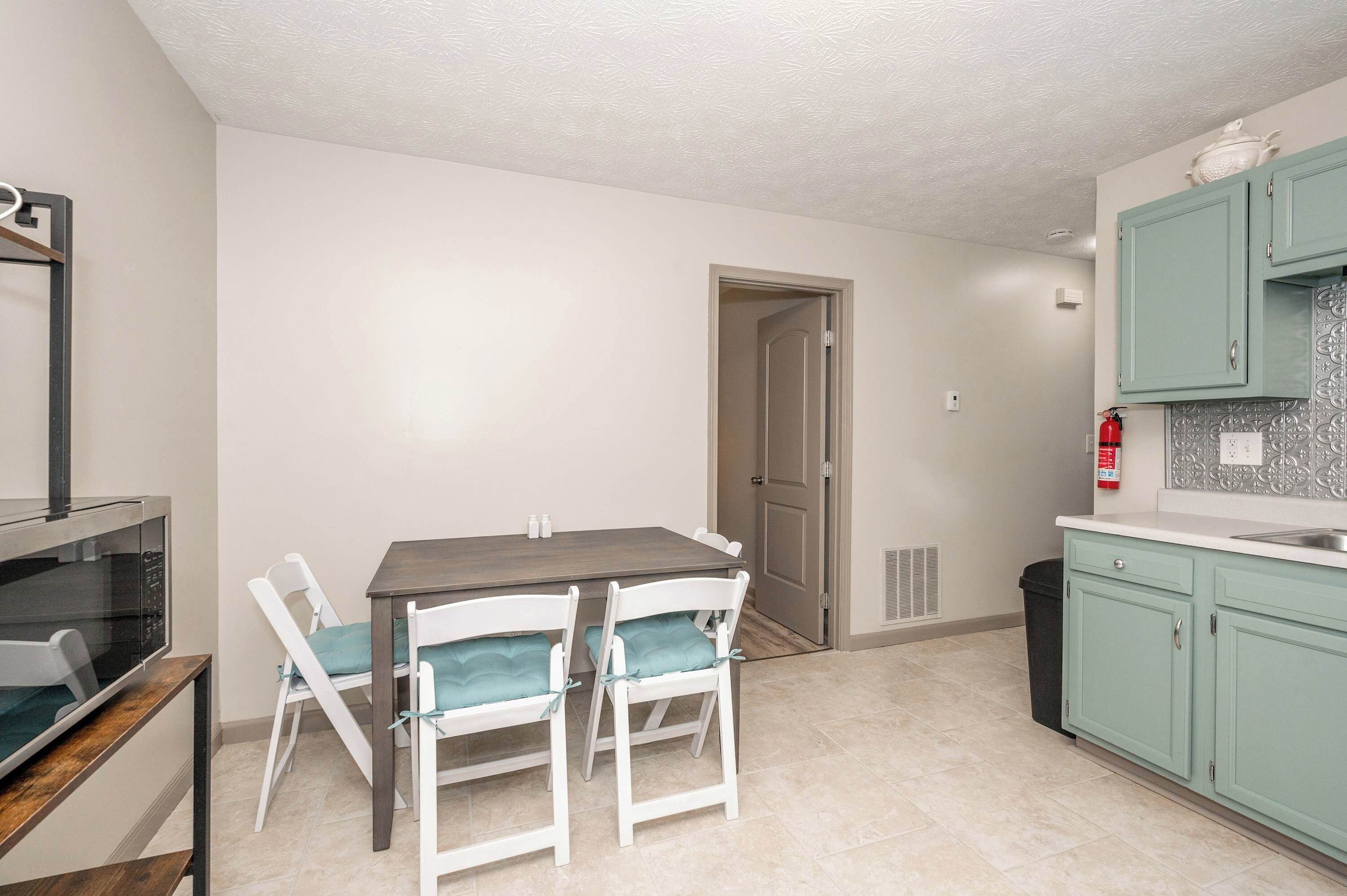 Una cocina compacta con una mesa de comedor y sillas, microondas, armarios y un extintor.