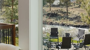 Ein Zimmer mit großem Fenster und Blick auf eine Terrasse mit Gartenmöbeln sowie eine Flusslandschaft.