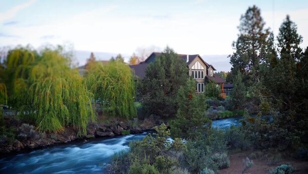 Ein Fluss fließt durch einen Wald, im Hintergrund steht ein Haus.