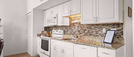 A kitchen with white cabinets, a microwave, stove, and a tiled backsplash.