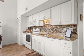 A kitchen with white cabinets, a microwave, stove, and a tiled backsplash. - Peaceful Lakeview Escape - For 6 (Branson)