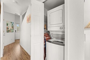 A laundry room with a front-loading washer and dryer, wooden flooring, and a door leading to another room. - Peaceful Lakeview Escape - For 6 (Branson)