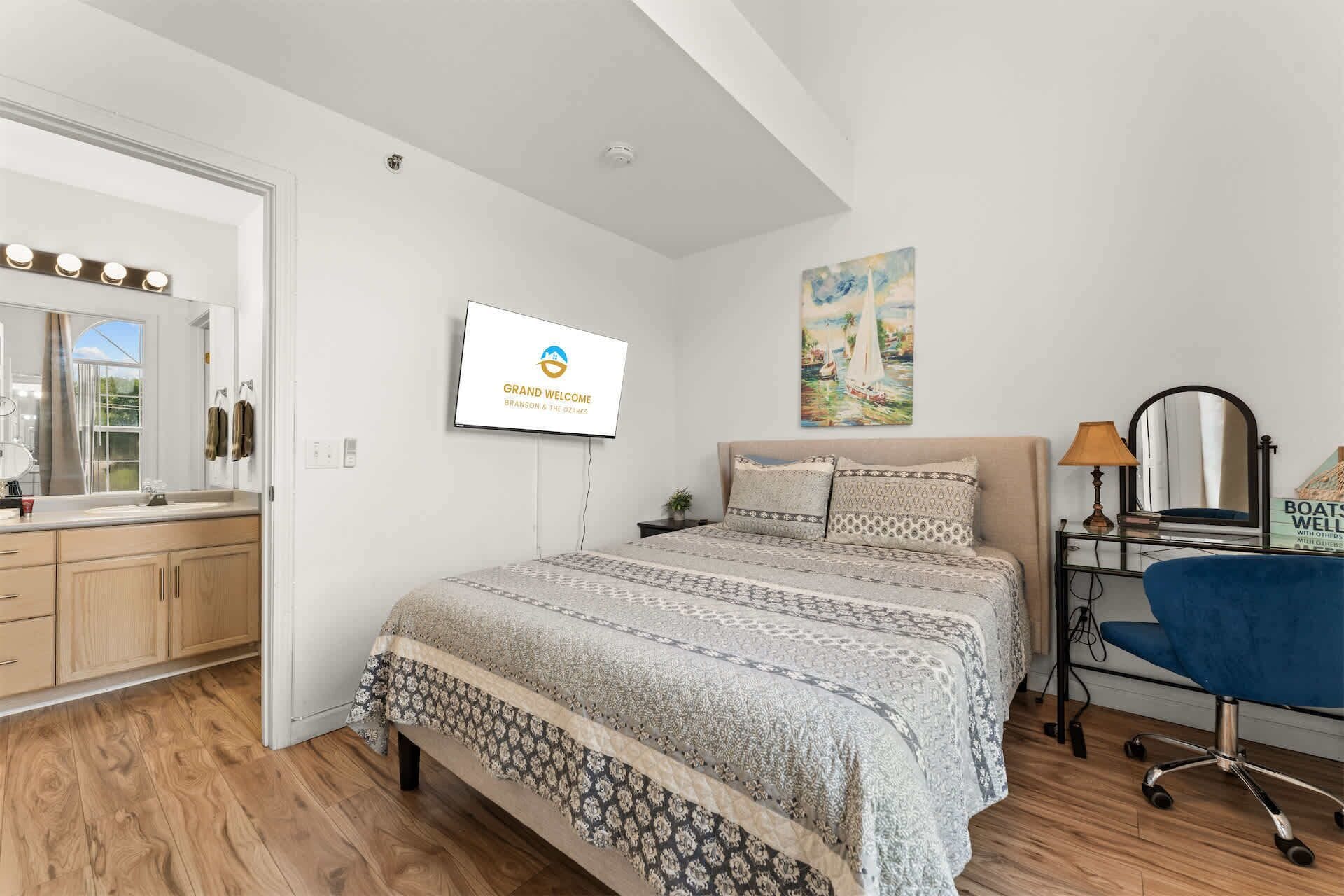 Ein Schlafzimmer mit Bett, Schreibtisch, Stuhl, Fernseher und einem Bild an der Wand.