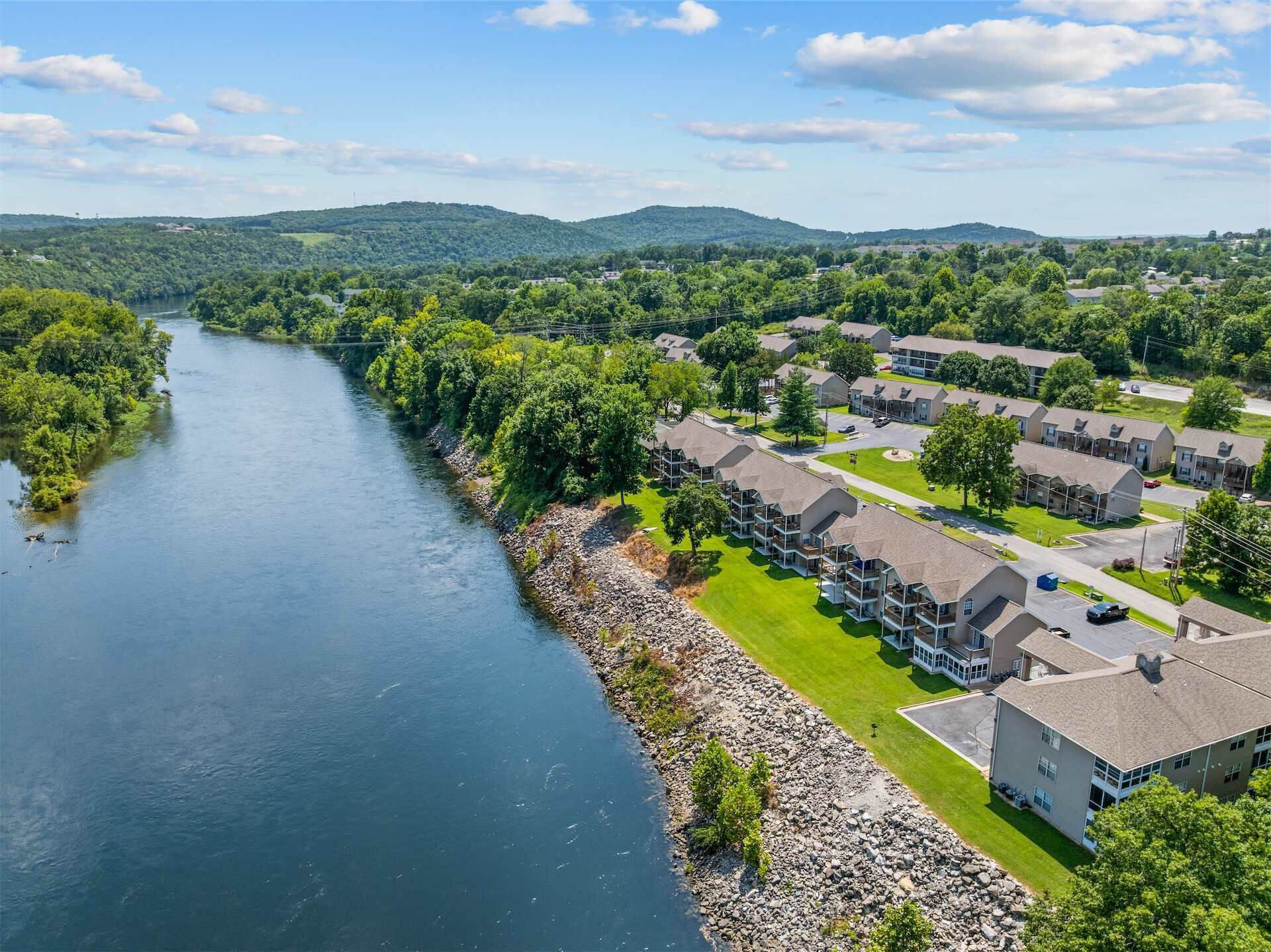 A riverside residential area with multiple-story buildings, a well-maintained lawn, and a clear view of the river.