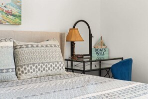 A neatly made bed with patterned pillows, a bedside lamp, a small table with a sign, and a blue chair. - Peaceful Lakeview Escape - For 6 (Branson)