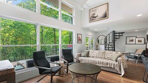 A spacious living room with large windows, a round table, and a sofa. - Treehouse LOZ Seclusion for 6! (Sunrise Beach)