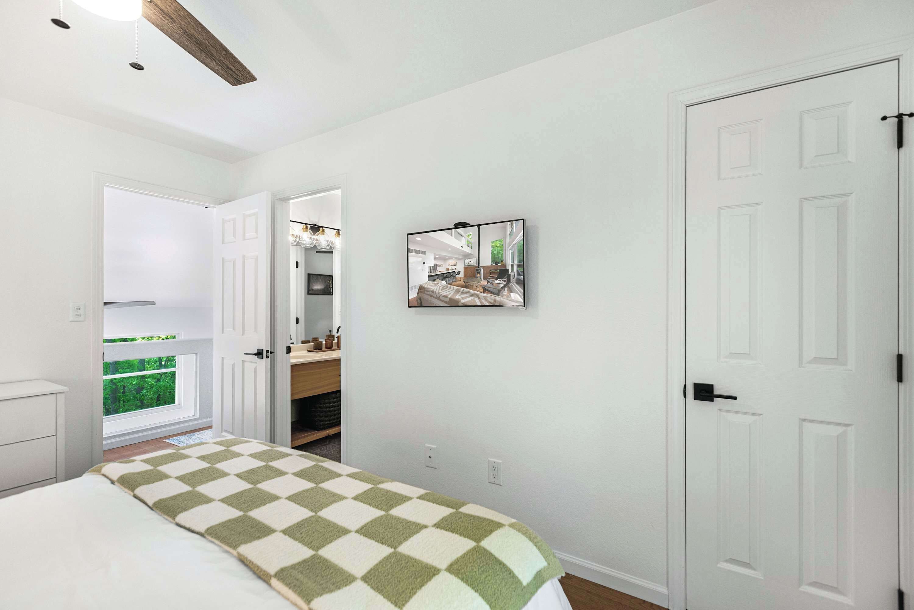 A bedroom with a bed, a door, a window, and a wall-mounted picture.