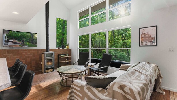 A modern living room with a fireplace, comfortable seating, and large windows offering a view of the outdoors. - Treehouse LOZ Seclusion for 6! (Sunrise Beach)