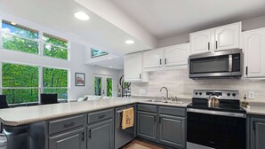 A modern kitchen with grey cabinets, a stainless steel microwave, and a black oven. - Treehouse LOZ Seclusion for 6! (Sunrise Beach)