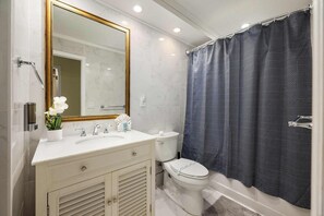 A bathroom with a white vanity, a large mirror, a toilet, and a shower curtain.