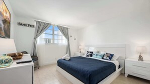 Een slaapkamer met een bed, nachtkastjes, een dressoir, een raam met gordijnen en een bord aan de muur.