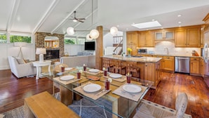 Un'ampia cucina con mobili in legno, un'isola centrale e un'area pranzo con tavolo in vetro apparecchiata per quattro persone.