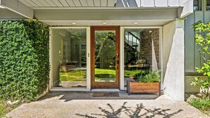 Ingresso di una casa moderna con porta in legno, porta in vetro e una piccola panca di legno all'esterno.