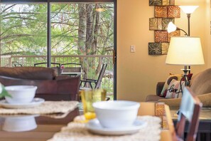 A cozy room with a balcony, furnished with a sofa, chairs, and a dining table set with bowls and cups. - Evergreen Haven - Golf, Attractions, & Amenities! (Branson)