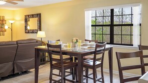 Un coin repas avec une table dressée pour quatre personnes, un canapé et une grande fenêtre donnant sur les arbres.