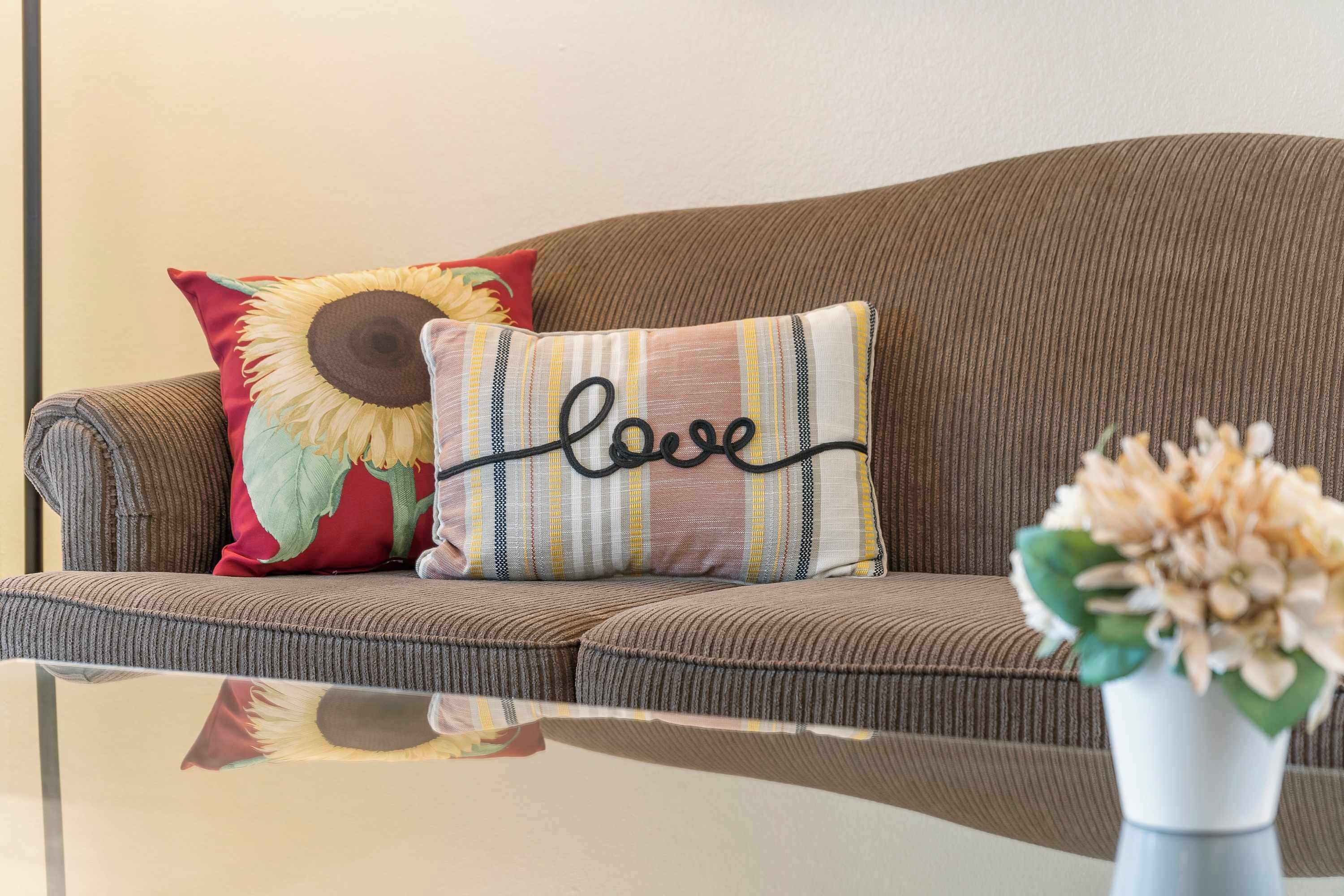 A brown sofa with striped cushions and a sunflower pillow with the word "love" on it.