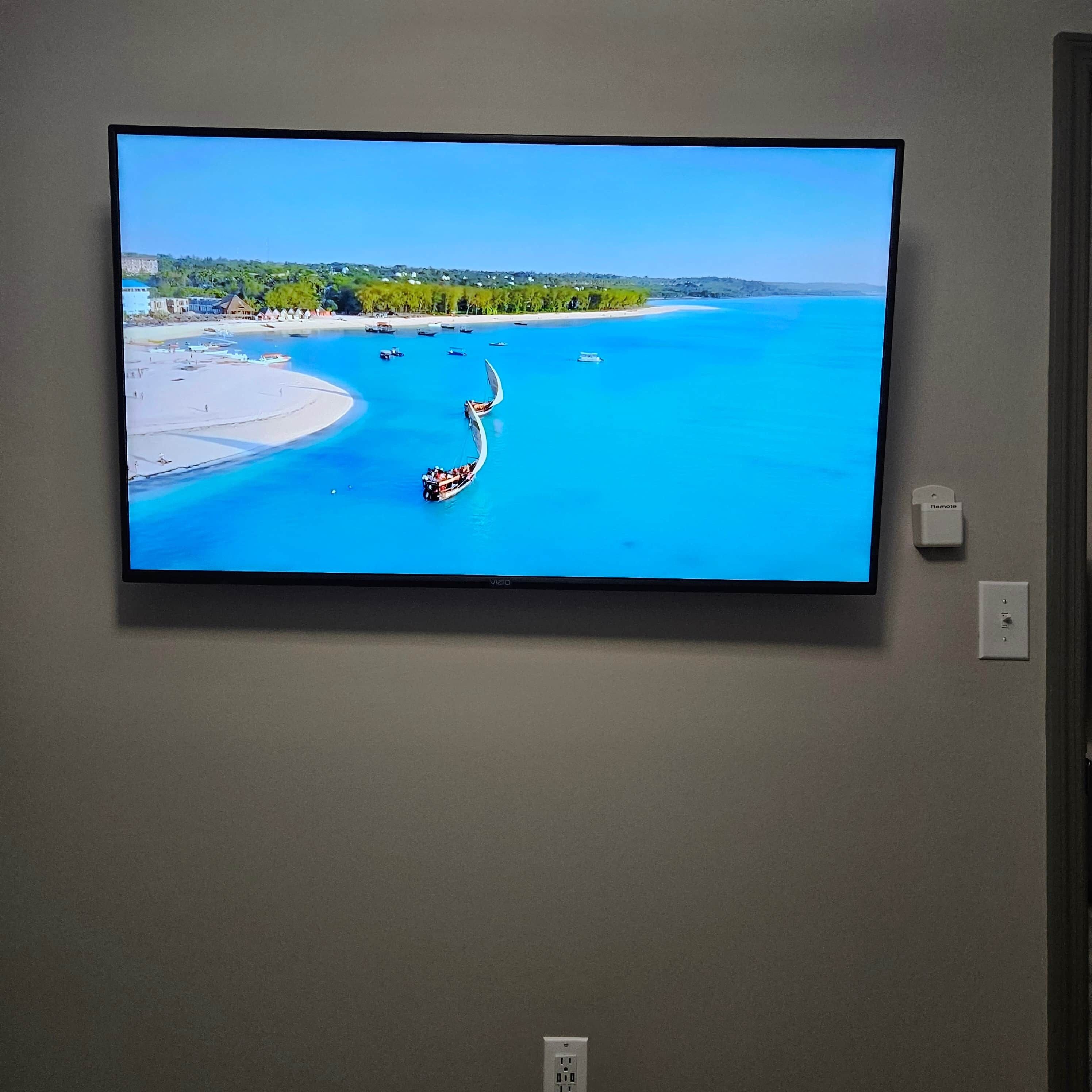 Un téléviseur à écran plat fixé au mur, diffusant une image d’un paysage côtier avec des bateaux et une plage.