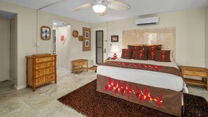 Une chambre à coucher comprenant un lit, une commode en bois, un ventilateur de plafond et un climatiseur fixé au mur.